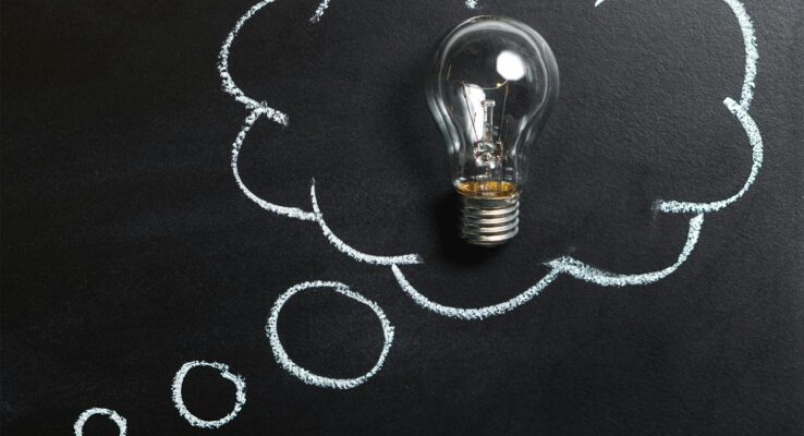 Light bulb laying on chalkboard with drawn thought bubble, symbolizing creative ideas.